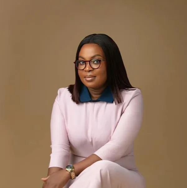 Mabel Adeteye seated in a pale pink outfit, wearing glasses