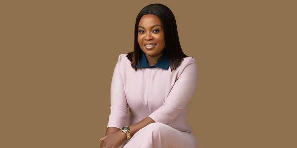 Mabel Adeteye seated in a pale pink outfit against a brown backdrop